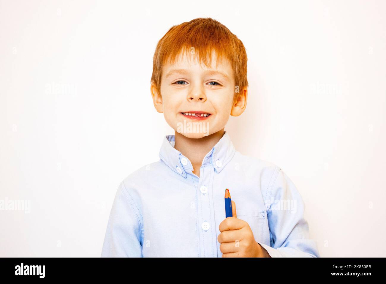 a little red-haired boy cheerful and thoughtful in a shirt with a pencil on a white background Stock Photo