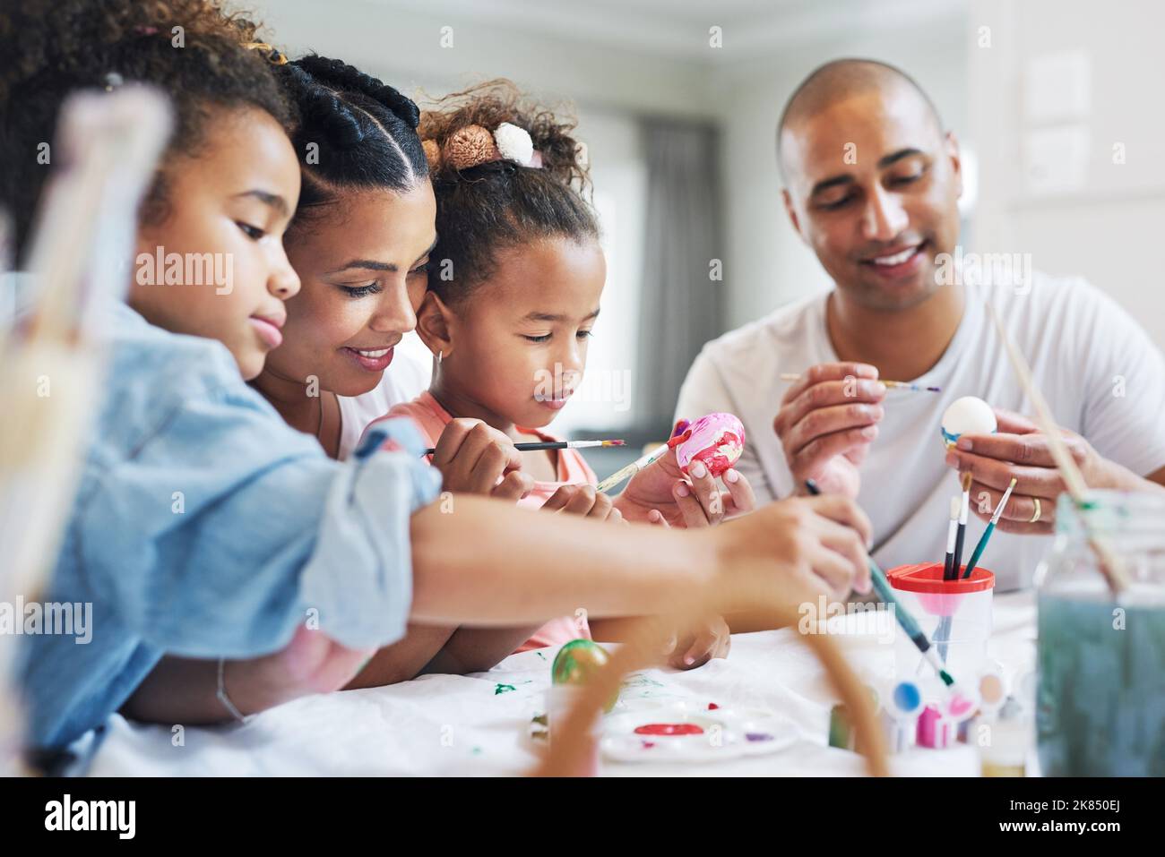 Seeing family is a important part of my weekend. a mother and father painting eggs with their daughter at home. Stock Photo