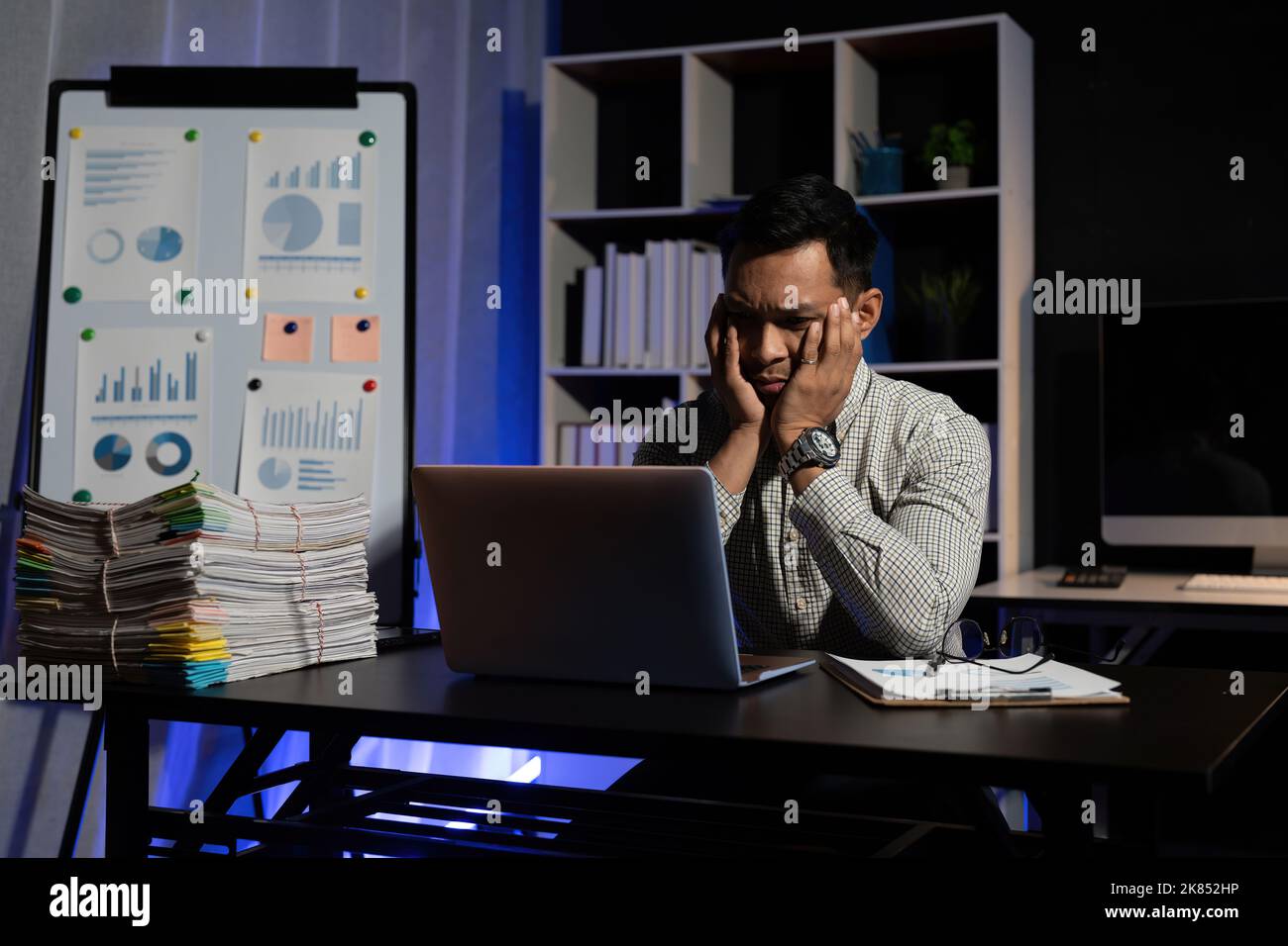 Tired or bored asian male worker sit at desk need rest suffer from fatigue overworked at office. Exhausted man working at computer late at night try Stock Photo