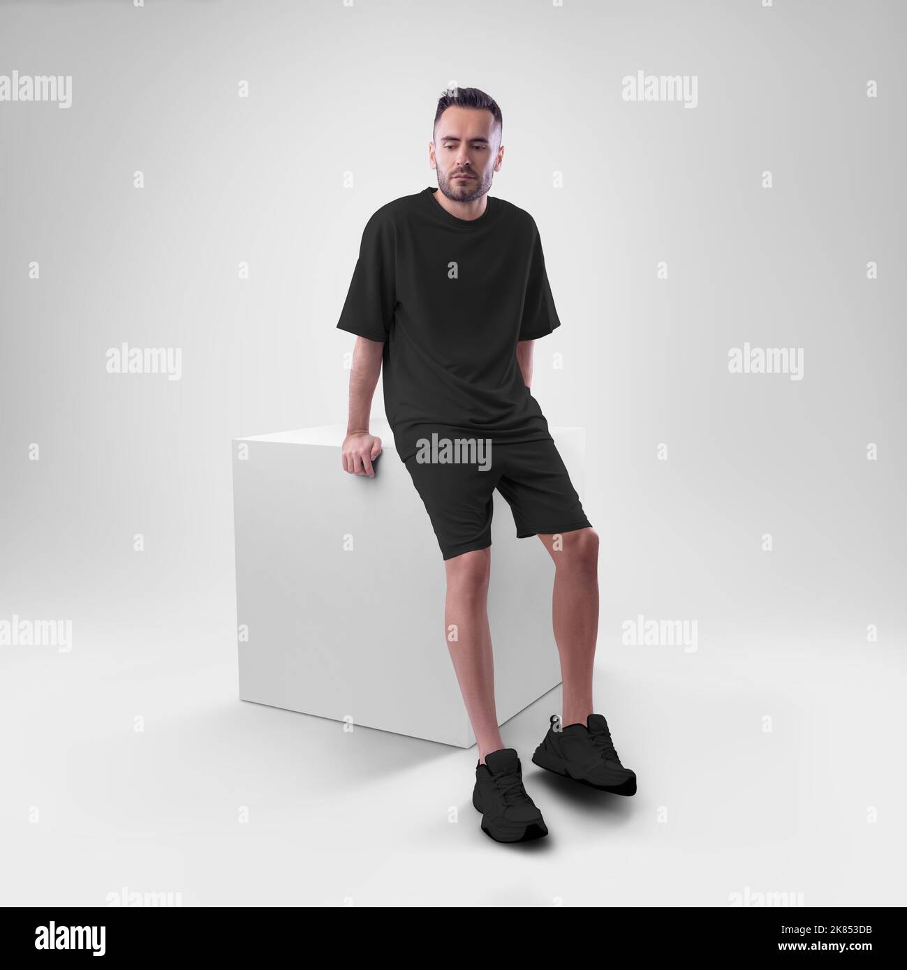 isolated mockup of trendy black men's oversized t-shirt with shorts on man sitting on cube. Clothing template for presentations of design, print, patt Stock Photo