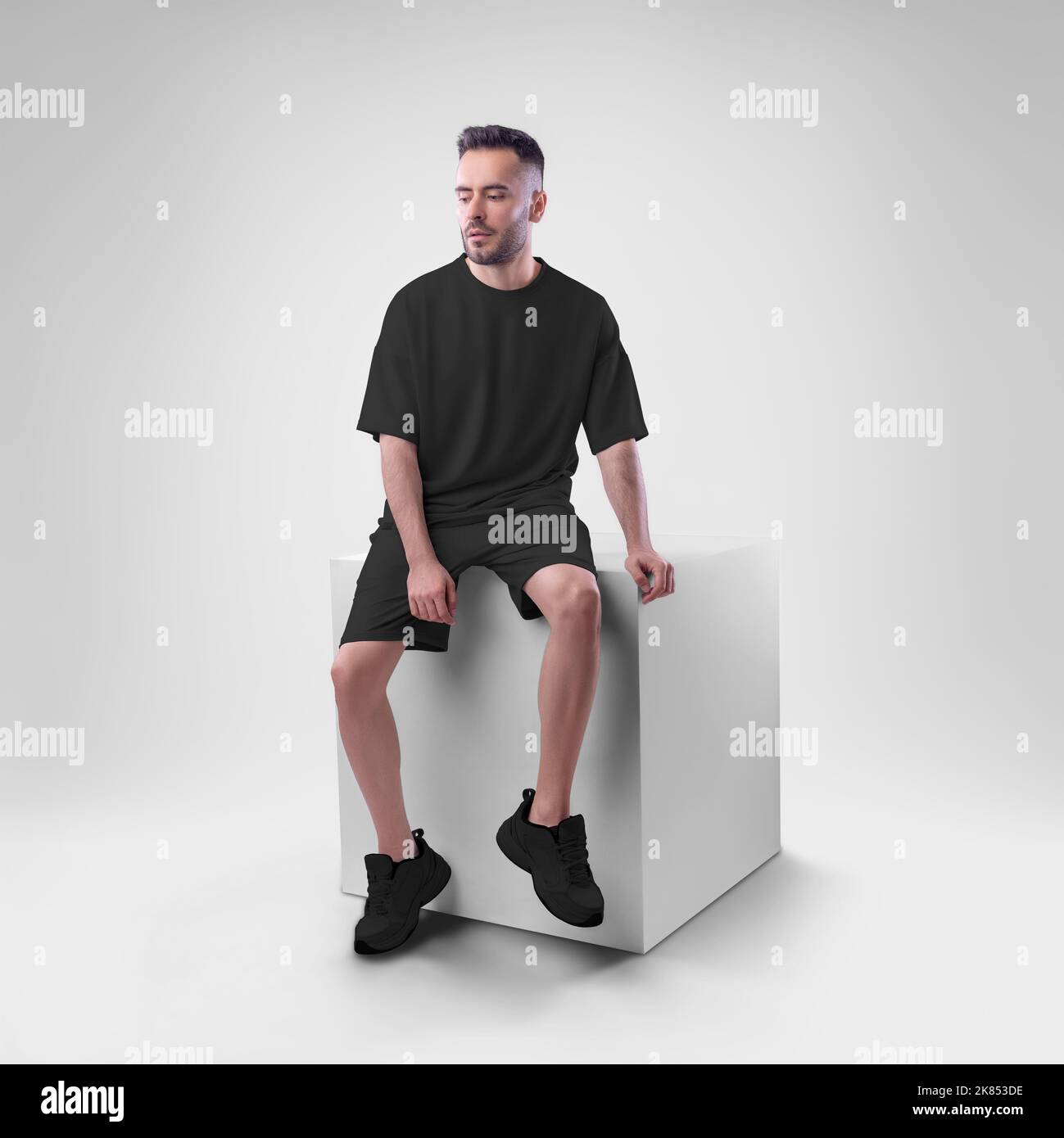 Mockup of black men's suit oversized t-shirt on shorts on man on cube. Clothing template for presentations of design, print, pattern. Stock Photo