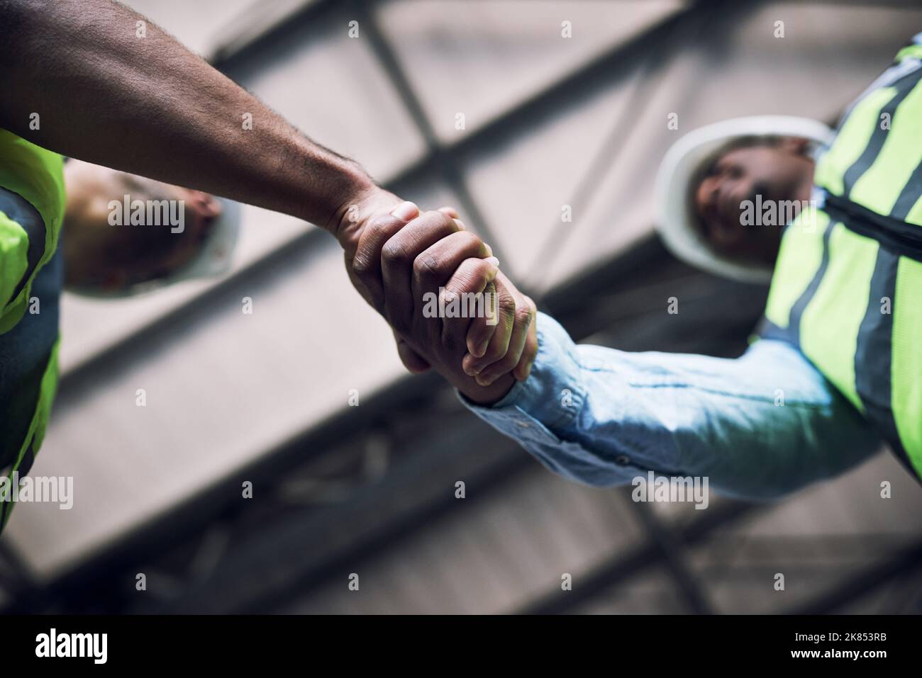 At the base of progress is teamwork. two builders shaking hands at a construction site. Stock Photo