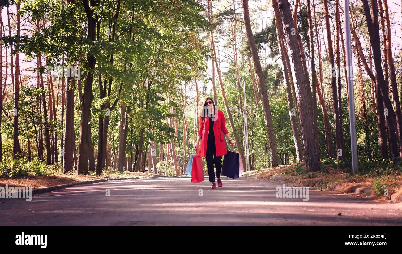 Woman with colored shopping bags in her hands, walking through city park. shopping and gifts. delivery or donation concept. High quality photo Stock Photo