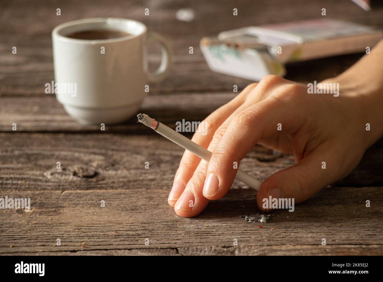 a cigarette in the hands of a girl on the table next to a cup of coffee