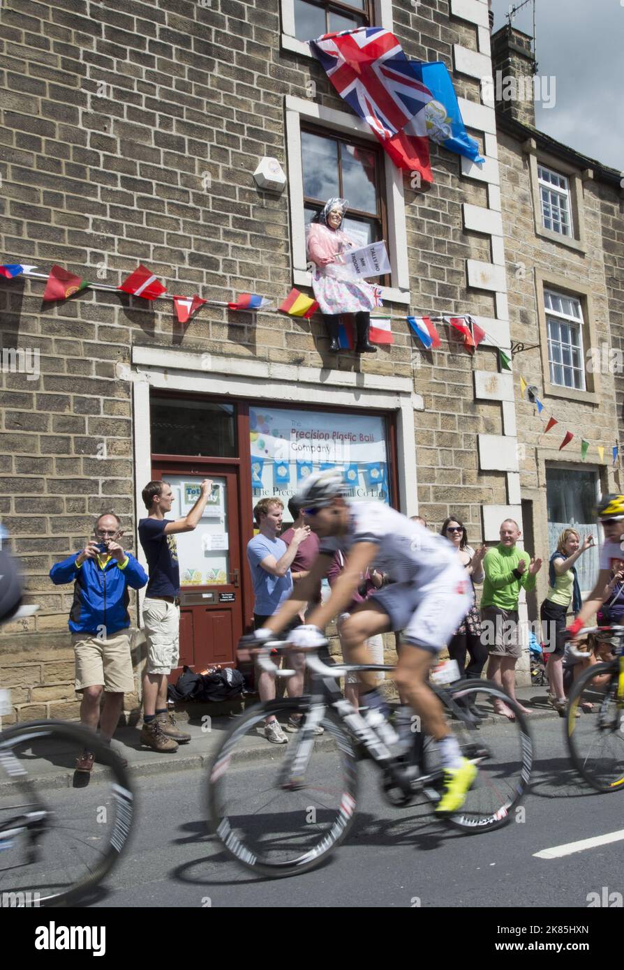 A doll looking like the Queen sits in a window as the peloton ride by with a sign saying Tallyhoo Mr Froome! Stock Photo