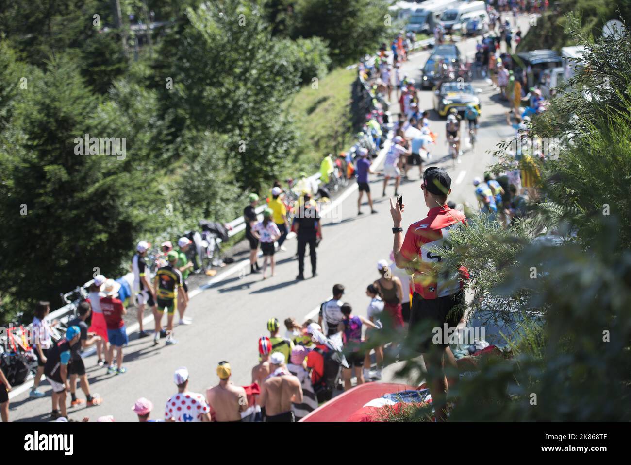 Three riders climb the final kms of the Col de Portillon with a spector on his phone during Stage 16 of the Tour de France 2018 from Carcassonne to Bagneres de Luchon.  Stock Photo