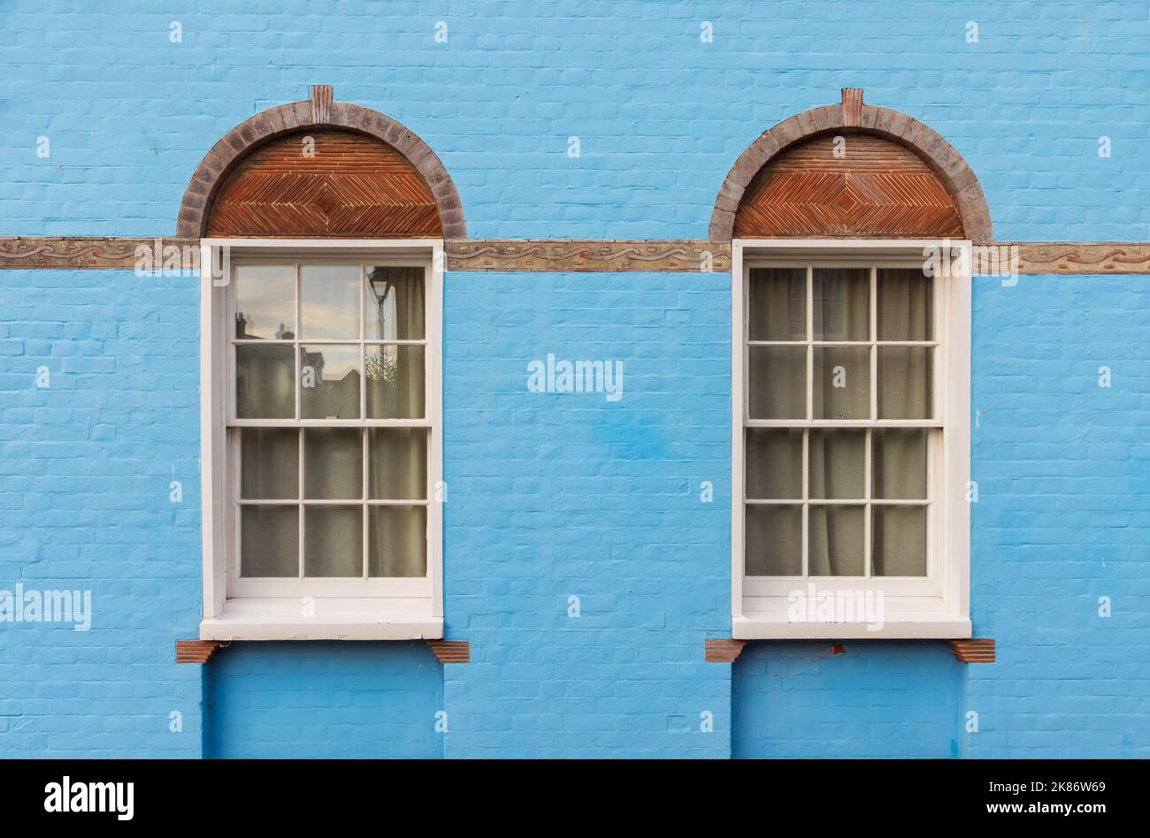 Side of an old house with blue brick wall with Victorian white wooden sash windows. UK Stock Photo