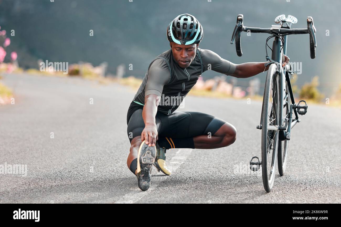 Outdoor, cycling and cyclist doing stretching exercise by his bicycle on road in mountain. Sports, training for fitness and man athlete doing warm up Stock Photo