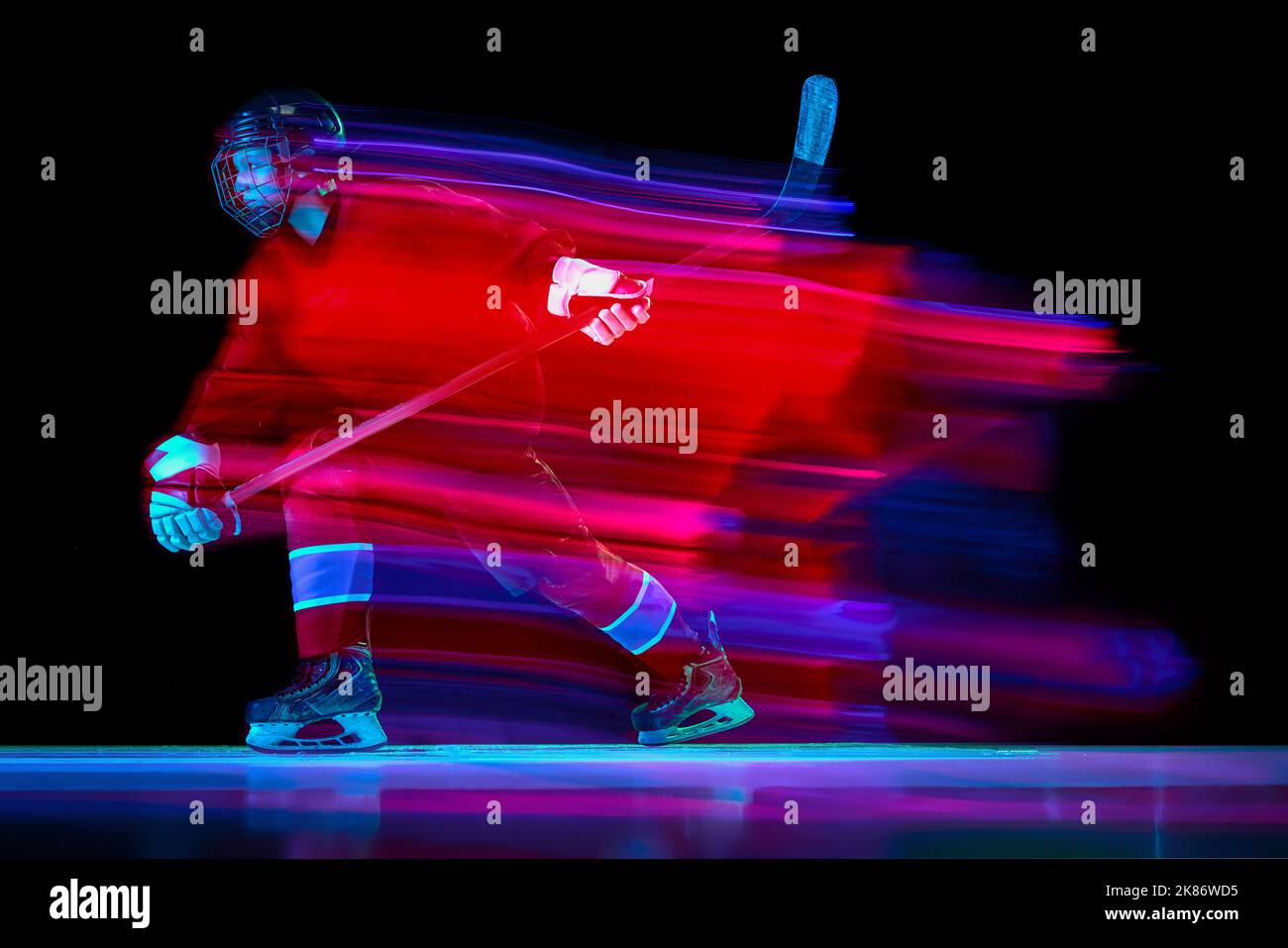 Dynamic portrait of energetic hockey player training with hockey stick isolated over dark background in mixed neon glow. Art, sport, action, motion Stock Photo