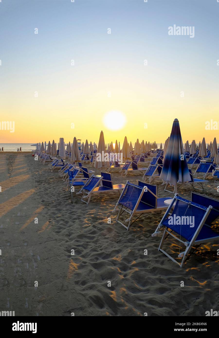 sun umbrellas and sun beds on the beach across sunrise sky. Pathway on ...