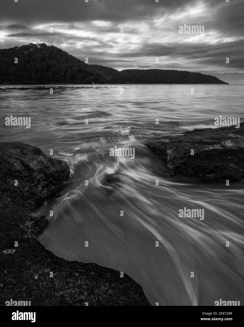 A grayscale shot of water flowing through rocks at Ettalong Beach in NSW, Australia Stock Photo