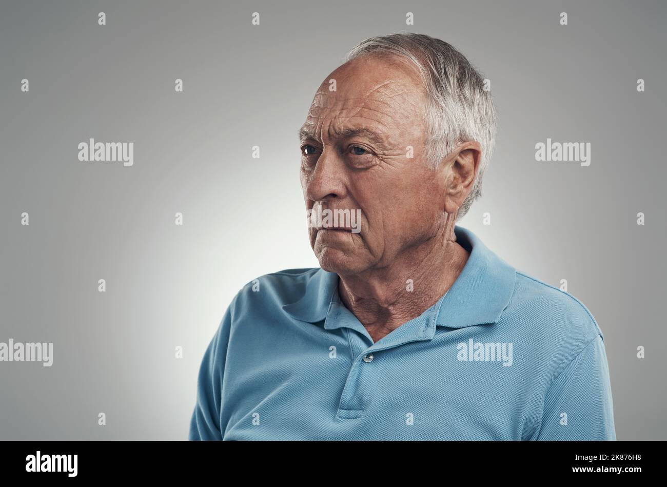 Today was a hard day. an older man looking off into the distance in a studio against a grey background. Stock Photo