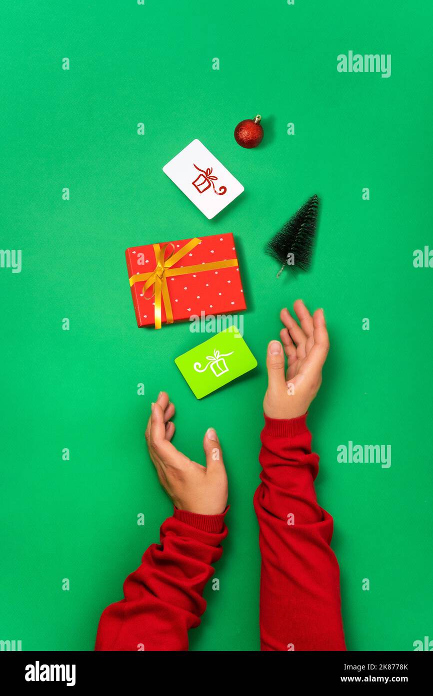 Minimal geen background, gift box, bonus and discount cards and Christmas objects in female hands. Concept of preparing and buying gifts for Christmas Stock Photo