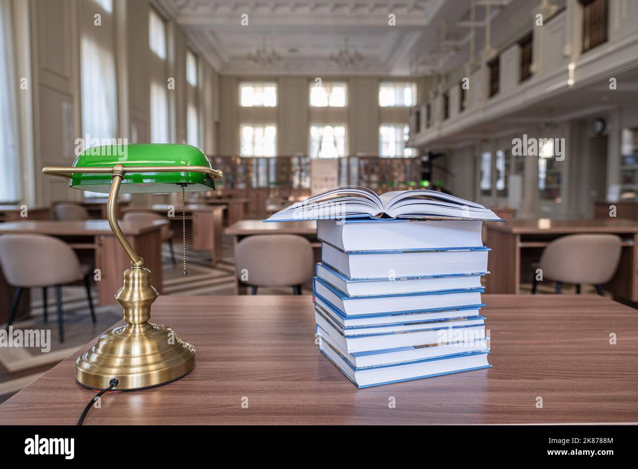 Book stack on wood desk and blurred bookshelf in the library room