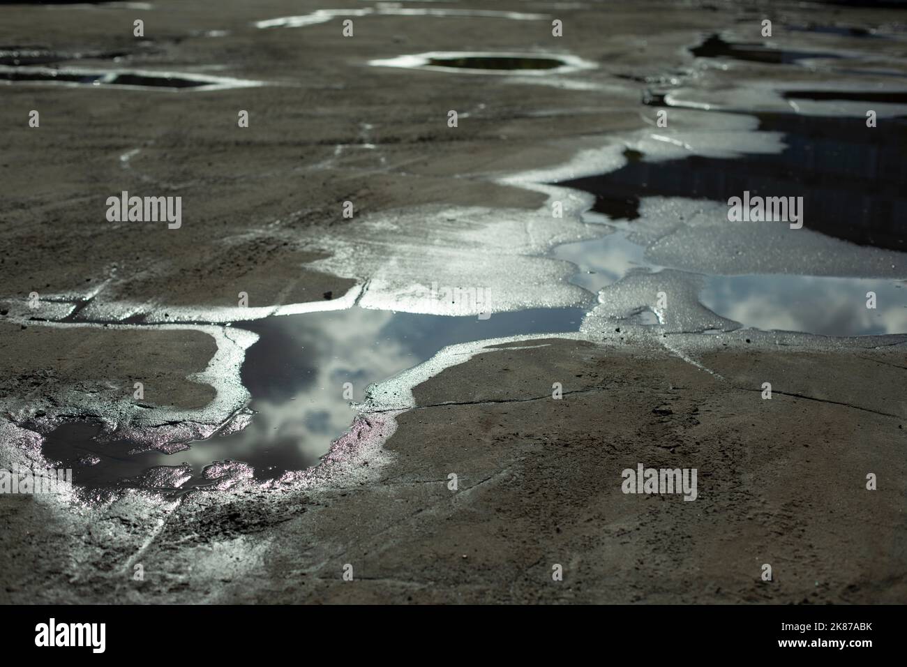 Large puddle on asphalt. Puddle after rain. Precipitation in city. Reflection of clouds in water. Stock Photo