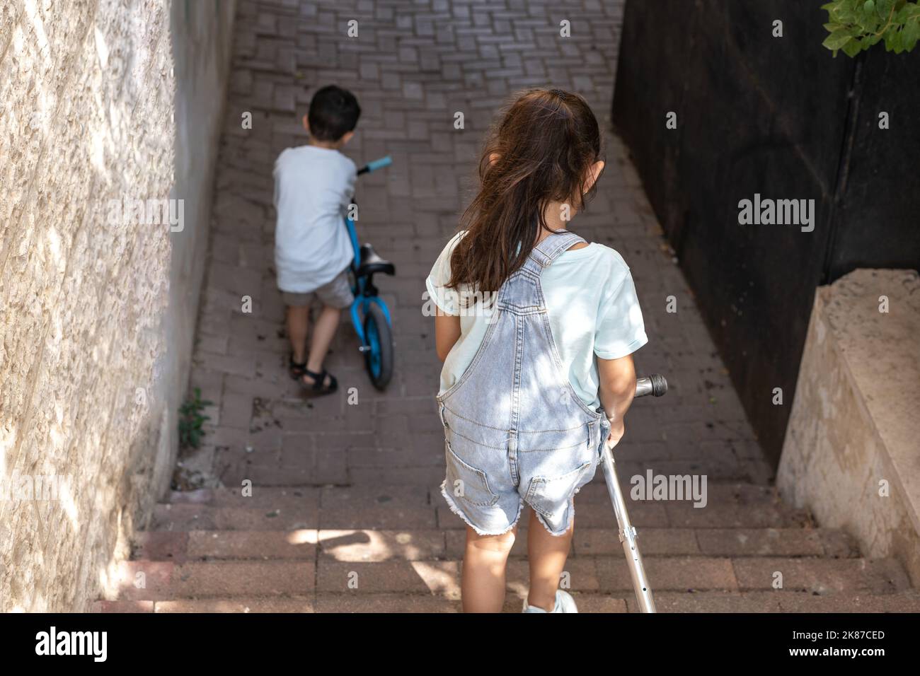 Boy with bicycle and his sister with scooter moving down on staircase in the city. Stock Photo