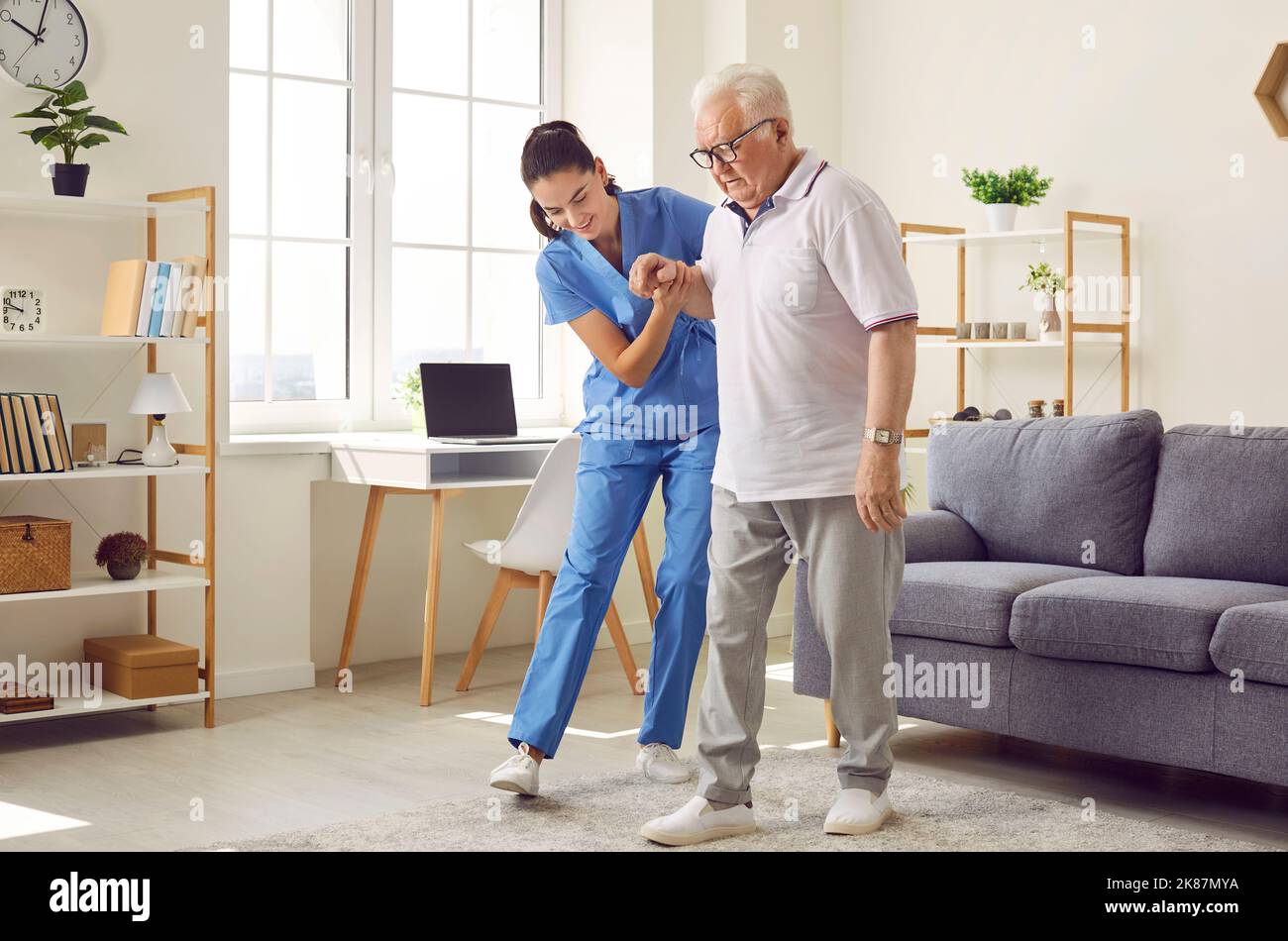 Nurse in assisted living facility holding elderly patient by hand and helping him walk Stock Photo