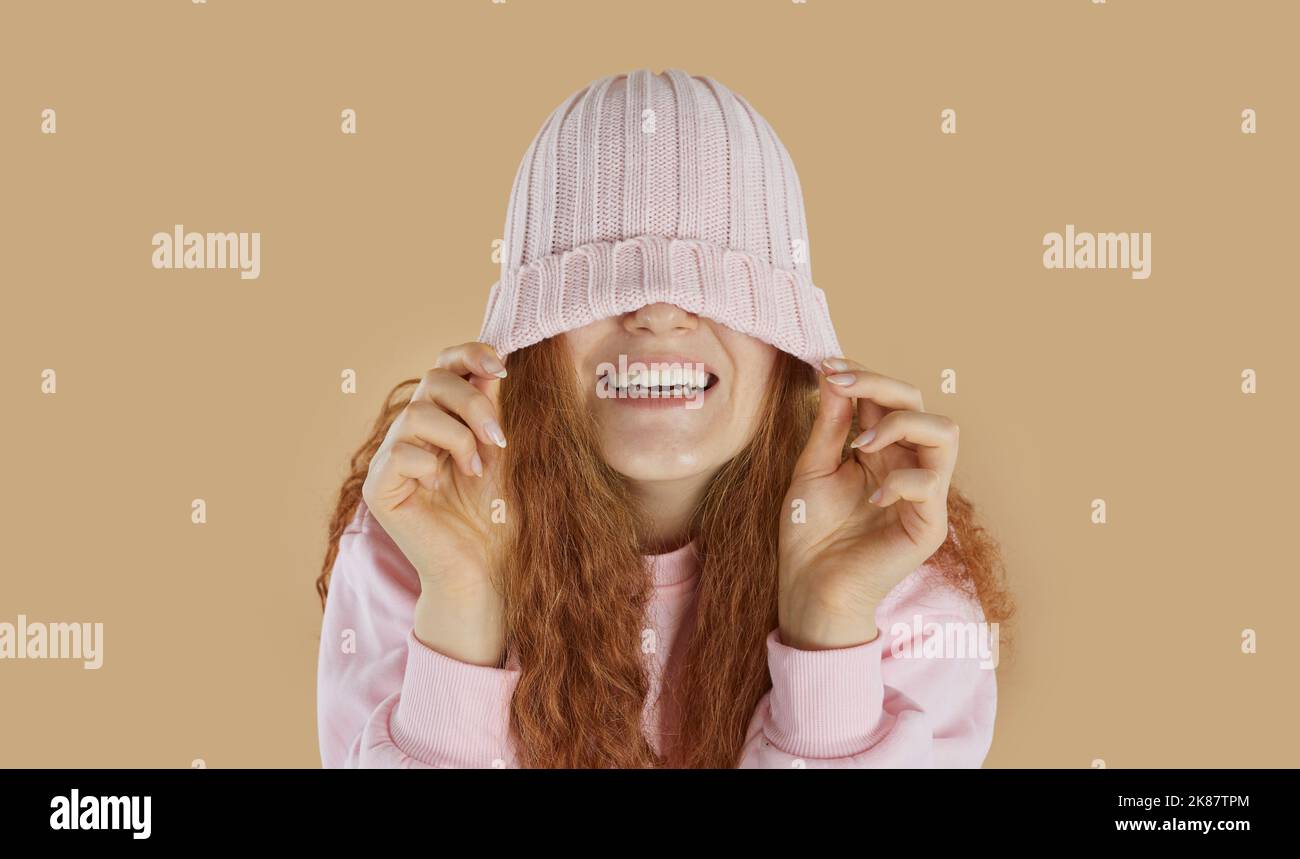 Laughing happy girl wearing in pink knitted hat pulled over the eyes on beige background. Stock Photo