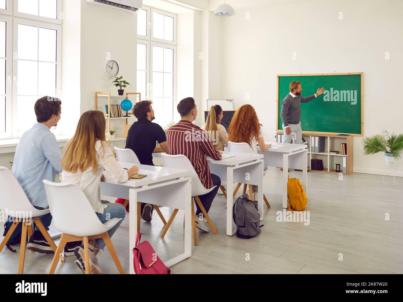 Group of students enthusiastically and attentively listens to professor explaining theme using green chalkboard. Stock Photo