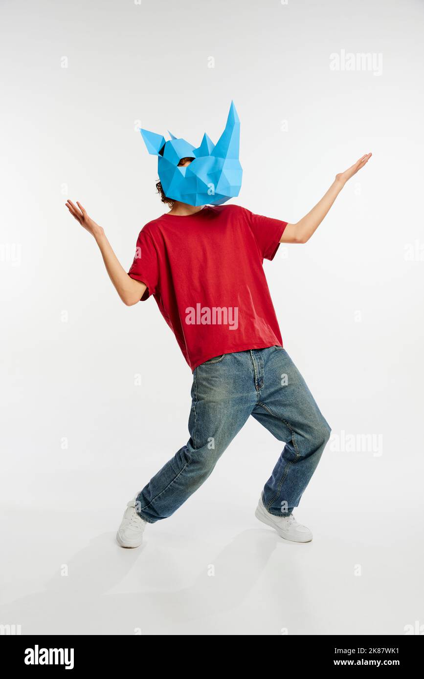 Dance. Young man in red t-shirt with cardboard animal mask on his head isolated on white background. Concept of art, fashion, theater, funny meme Stock Photo