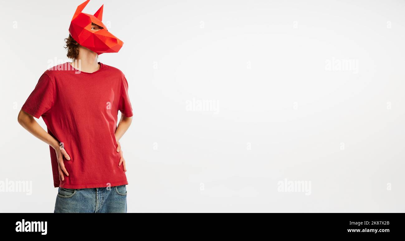 Young man in red t-shirt with cardboard animal mask on his head isolated on white background. Concept of art, fashion, theater, funny meme emotions. Stock Photo