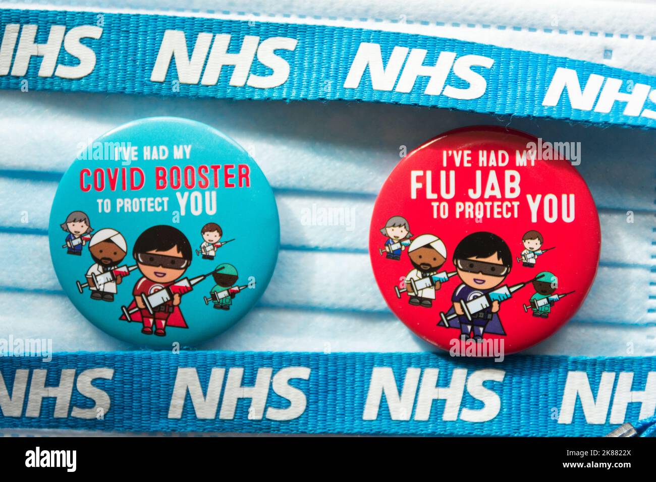 Colourful Covid 19 Booster and Flu Jab badges laying next to a NHS lanyard and surgical face mask Stock Photo