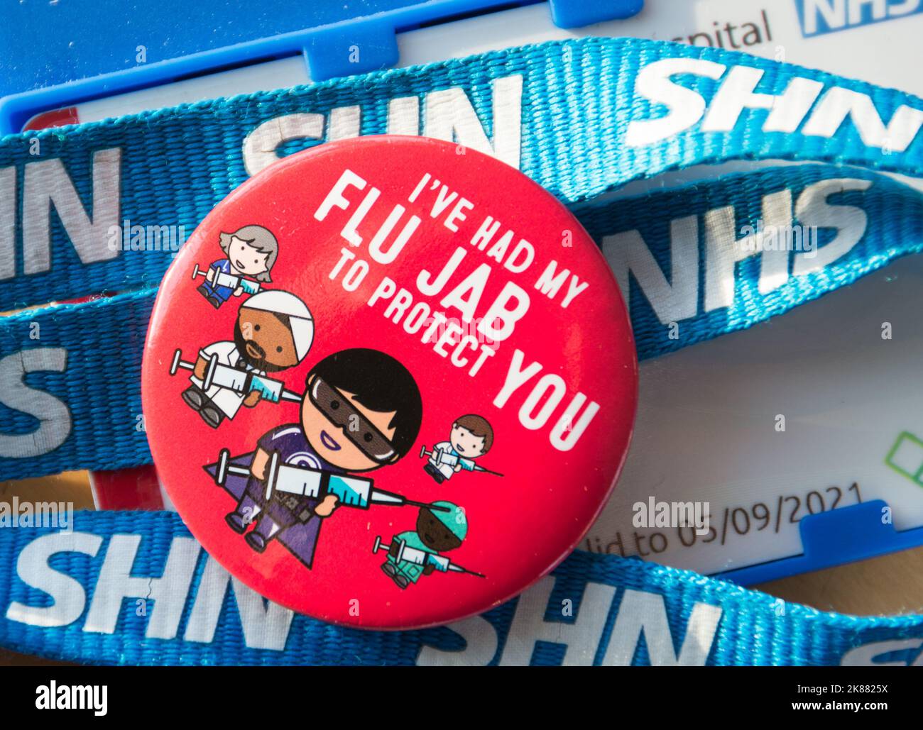 A colourful red flu jab badge resting on top of blue NHS lanyards Stock Photo