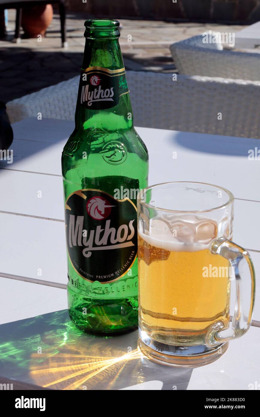 Single Green Mythos Greek beer bottle and glass of Mythos partially