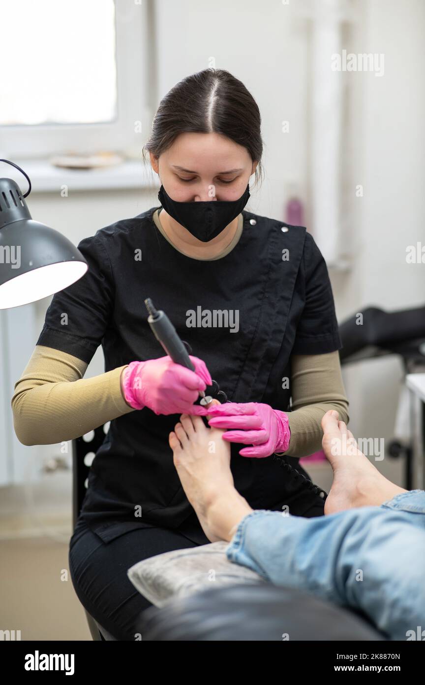 The pedicure master processes the client's foot using an apparatus with an abrasive disc. Stock Photo