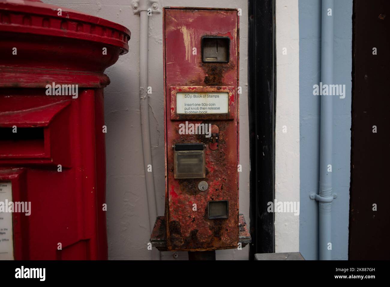 A rusty, defunct machine selling 50p books of stamps, next to a post box, October 2022. Stock Photo