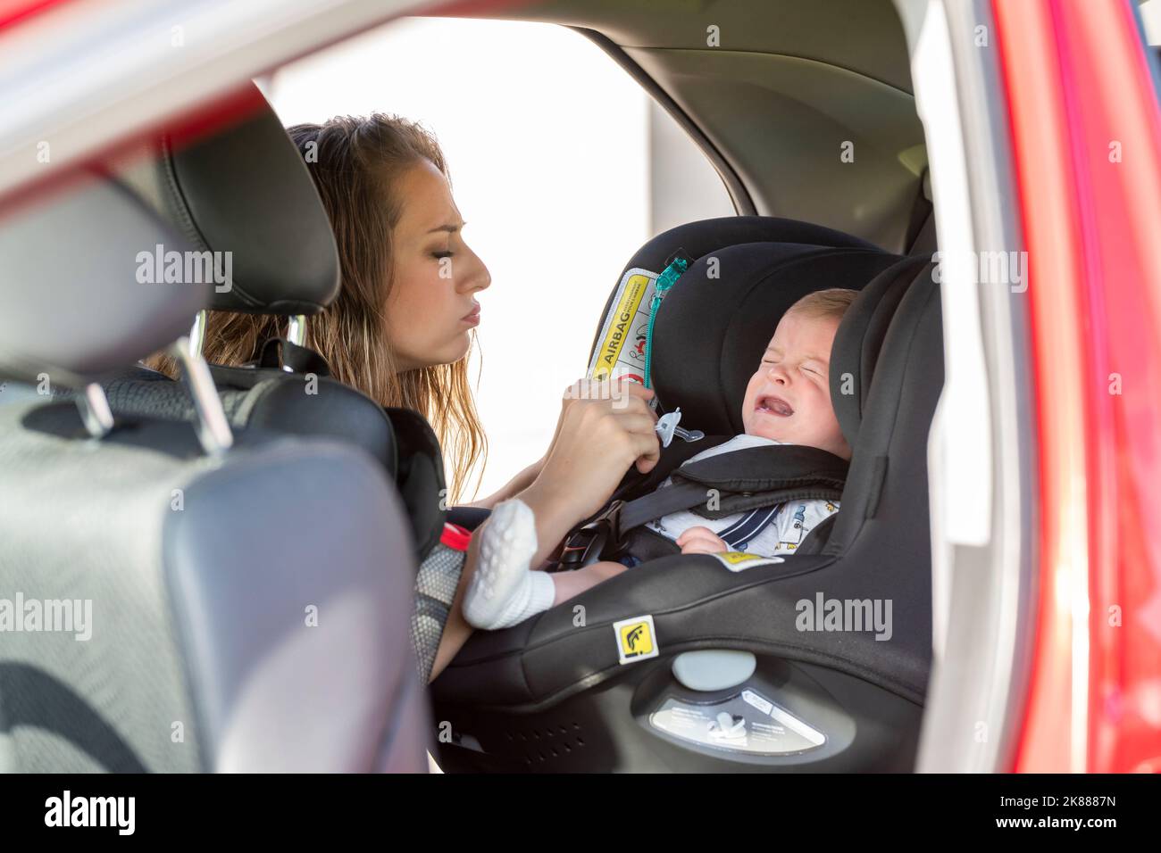 stressed mother with her crying baby in the back of the family car Stock Photo