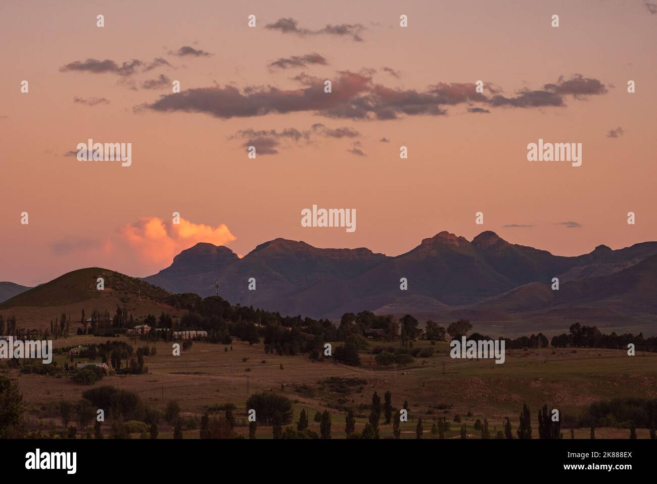 A view of the mountains under an orange sky at sunset in Clarens, South Africa. The popular town is near the Golden Gate Highlands National Park, whic Stock Photo