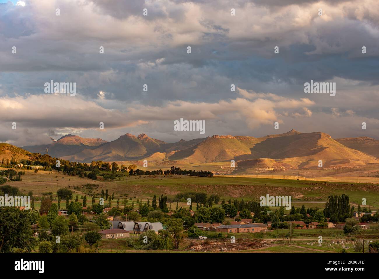 A view of the mountains lit up in gold under a stormy sky at sunset in Clarens, South Africa. This popular tourist destination is near the Golden Gate Stock Photo