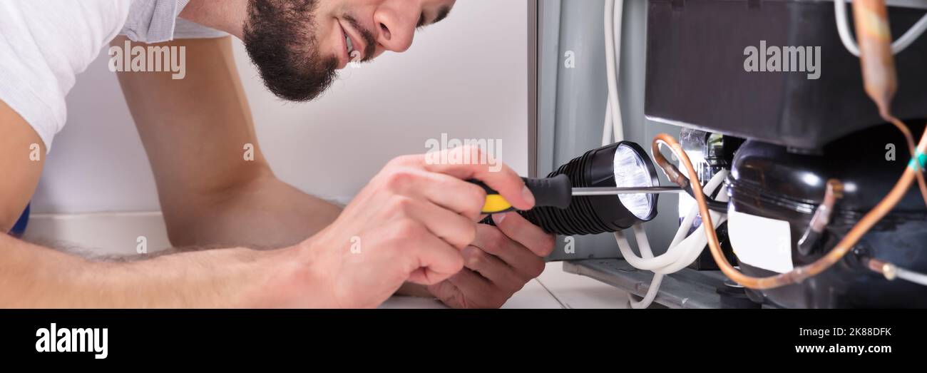 Fridge Appliance Repair At Home. Man Fixing Refrigerator Stock Photo