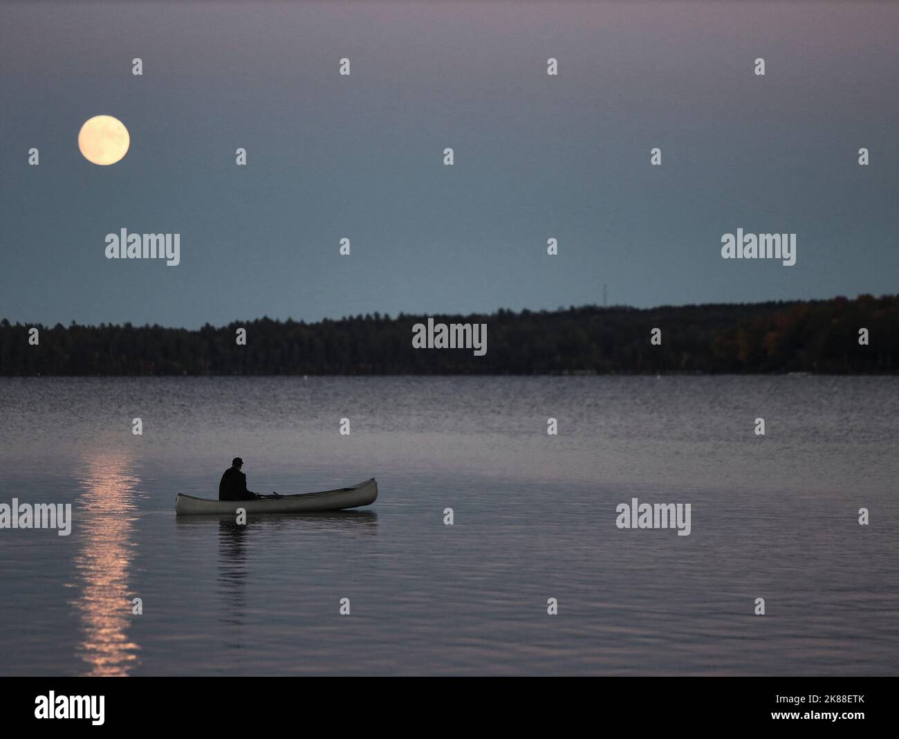 Solitary canoe paddle under a full moon on Sebec Lake in Maine Stock