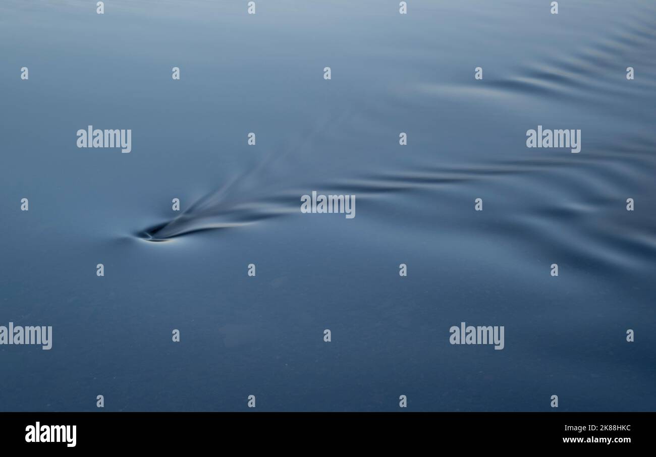 Smooth water rippling as it passes over a submerged rock Stock Photo