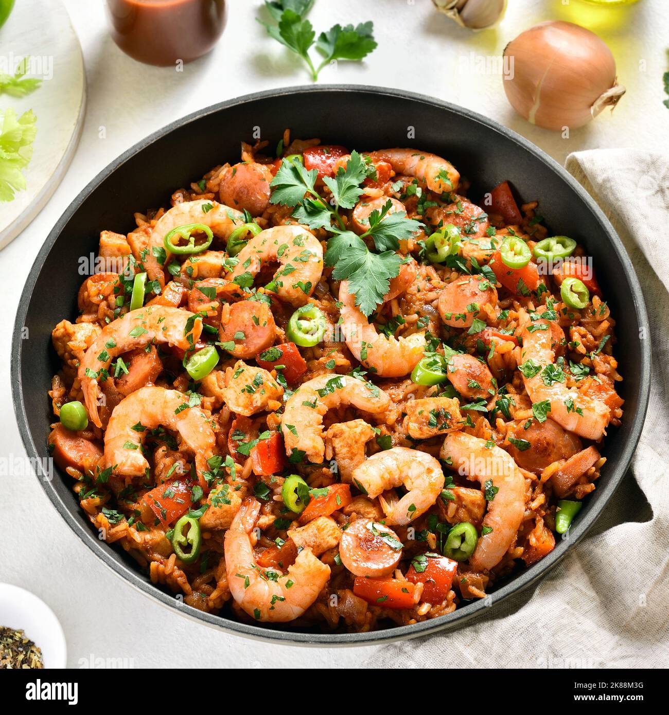 Creole jambalaya with chicken, smoked sausages and vegetables in frying pan on white stone background. Close up view Stock Photo