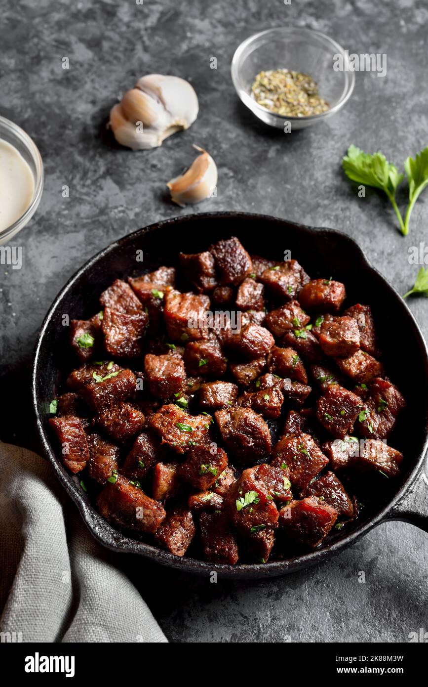 Garlic butter steak bites in cast iron pan on stone background. Close
