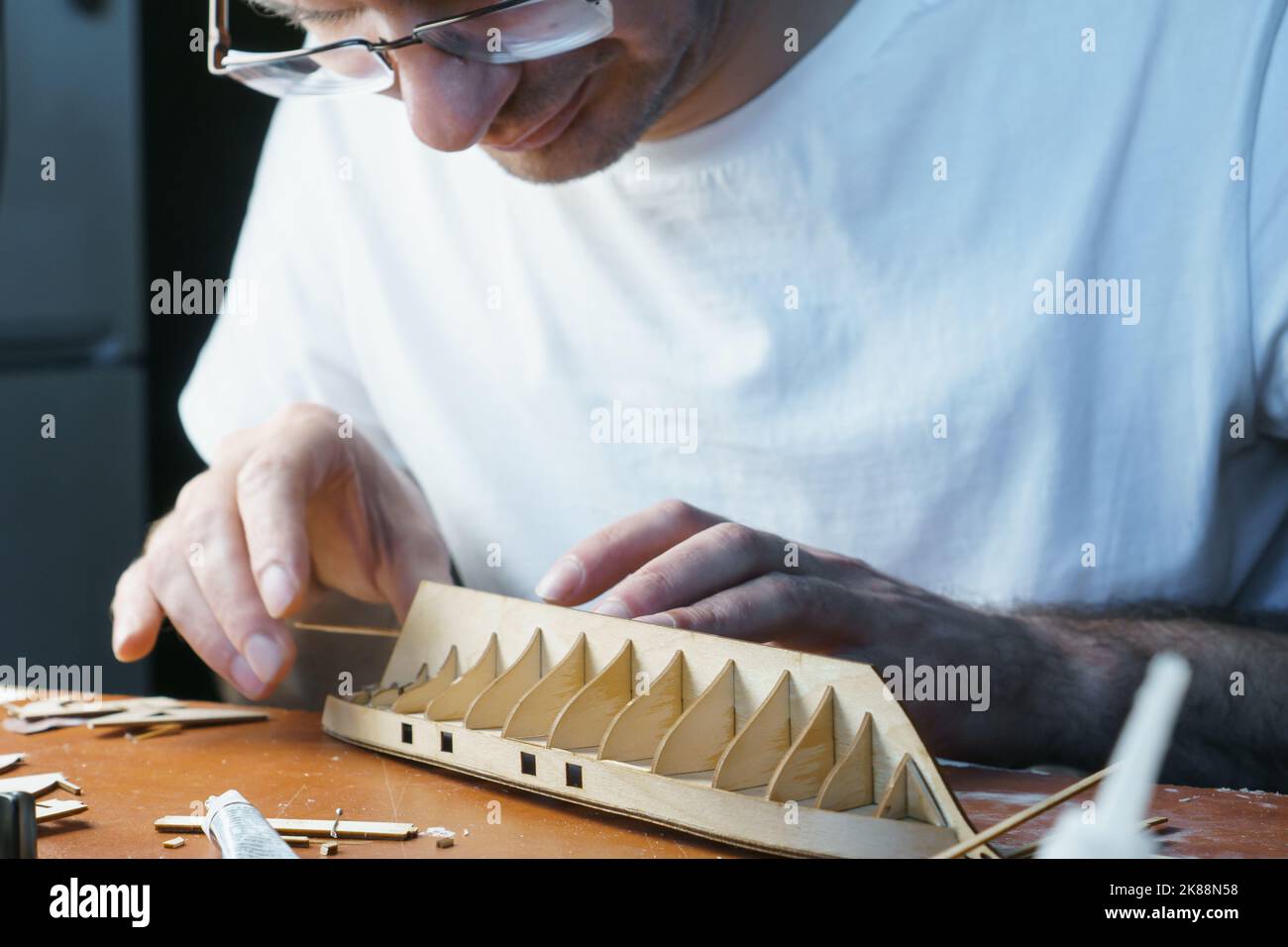 Hands of man gluing plywood details for ship model with glue, holding