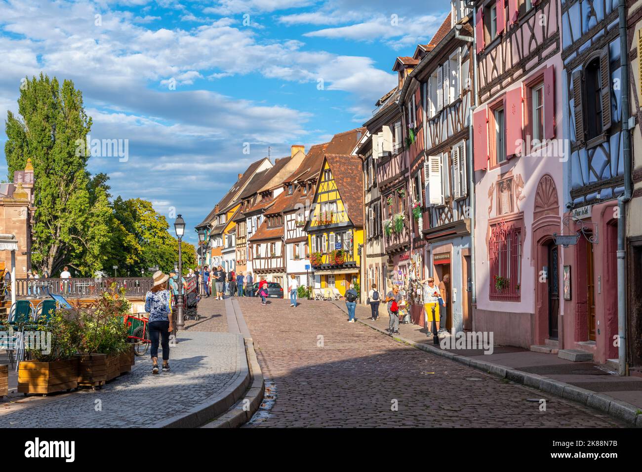 A picturesque street of shops and sidewalk cafes in the medieval old town of Colmar, France, one