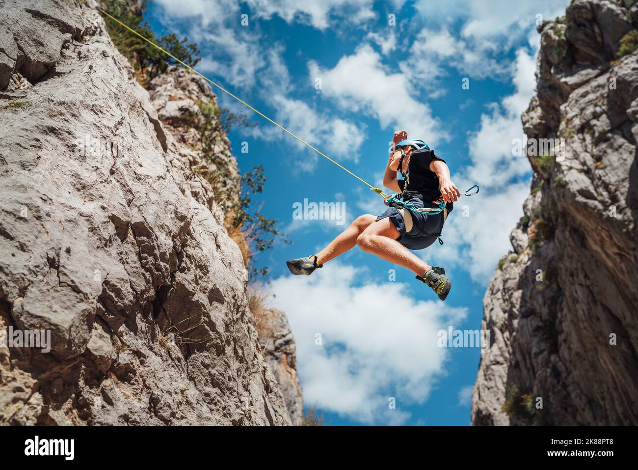 Climber teenage boy in protective helmet jumping on vertical cliff rock
