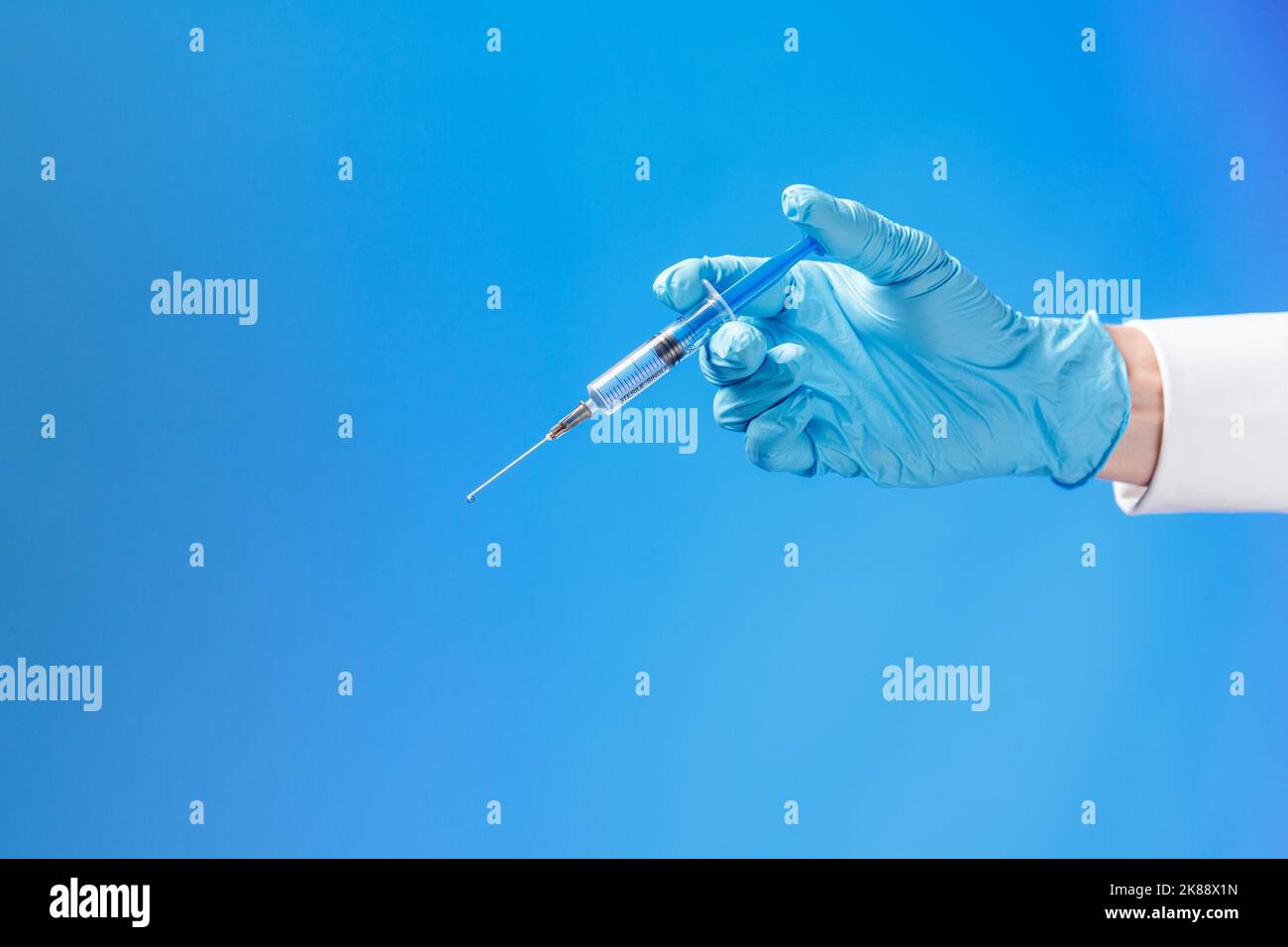 Hand in a blue rubber glove holding a syringe ona blue background ...
