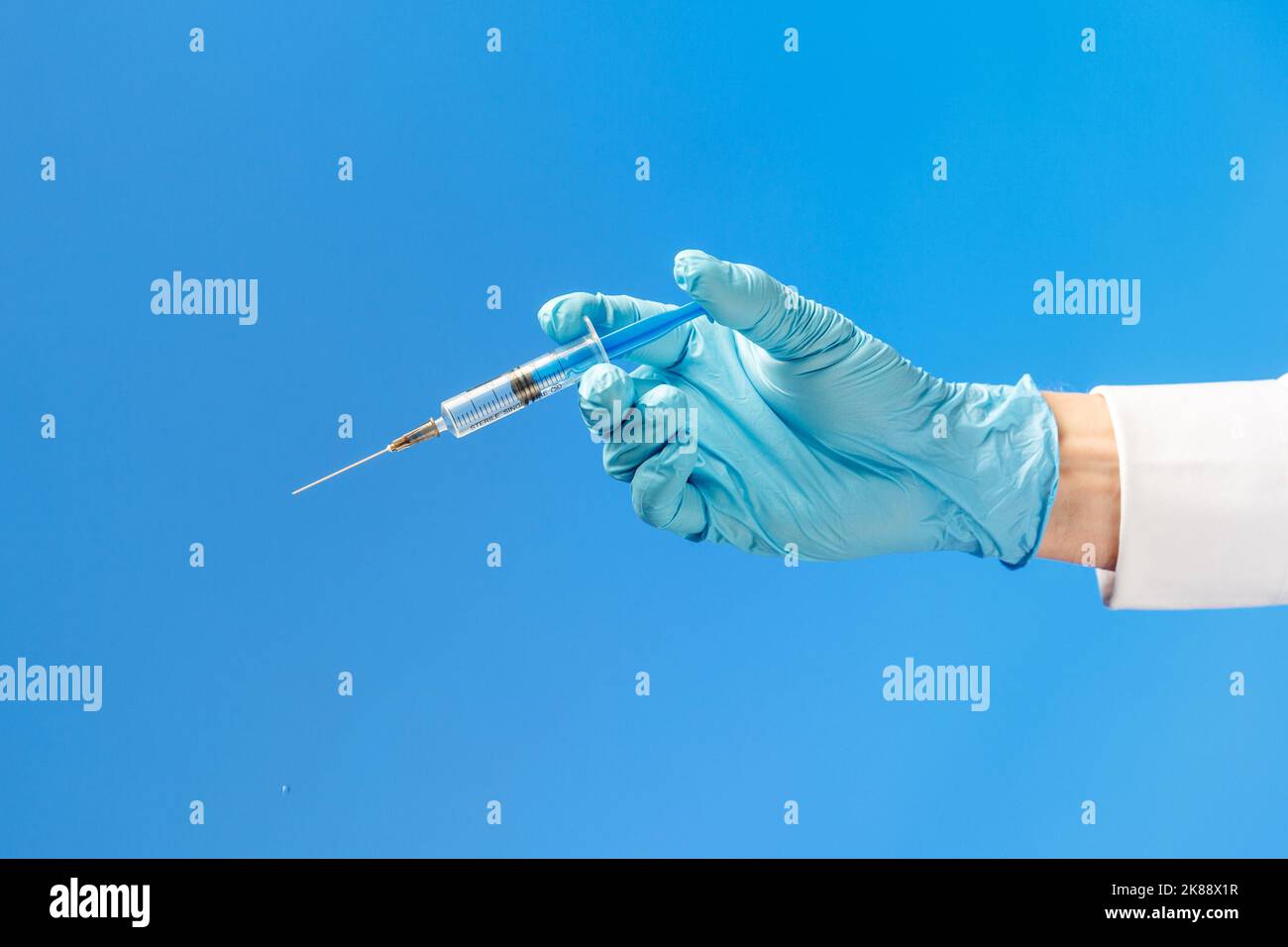 Hand in a blue rubber glove holding a syringe ona blue background ...