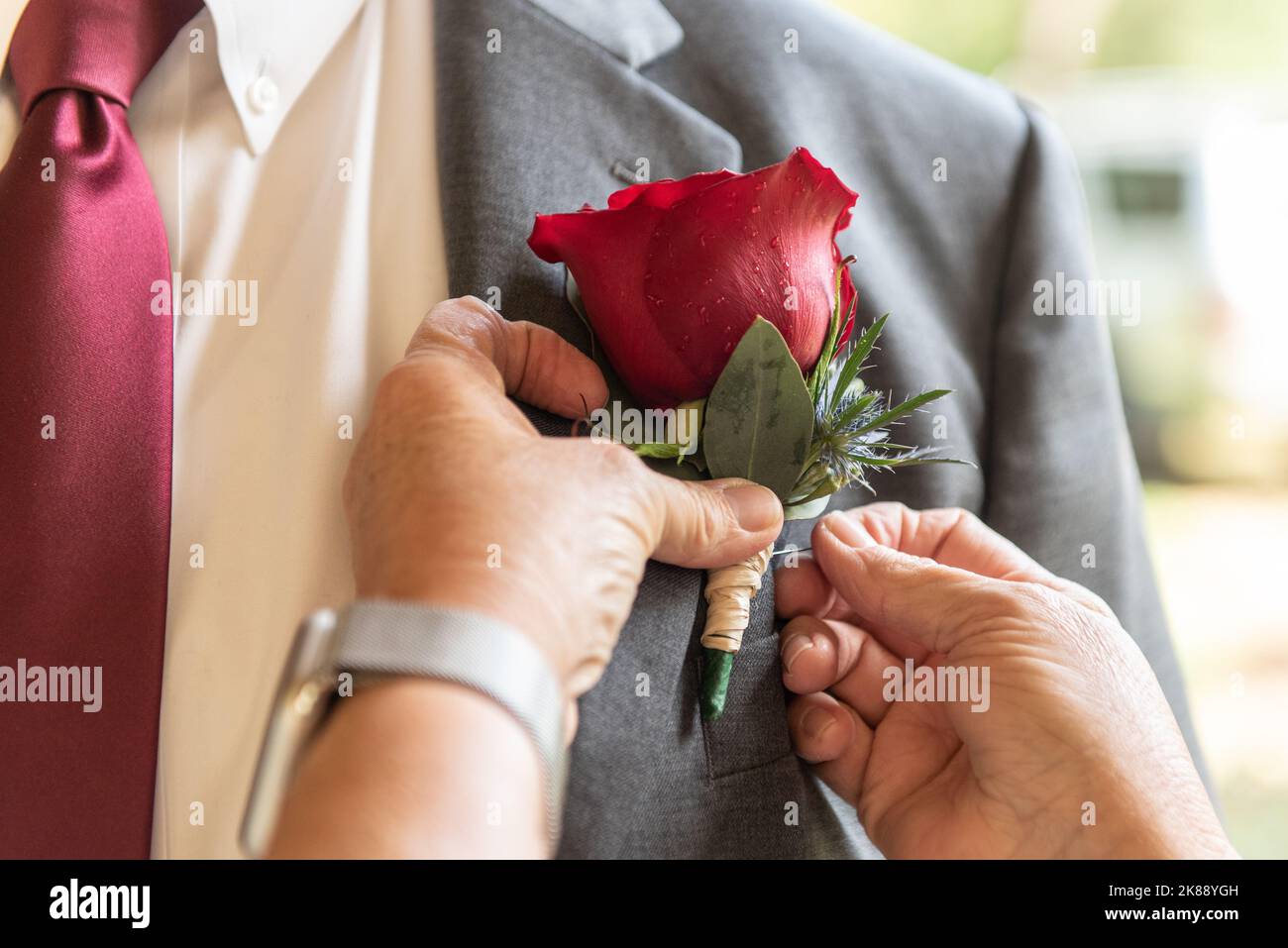 Hands helping pin the boutonniere onto the lapel of his suit jacket by pushing with the thumbs. Stock Photo