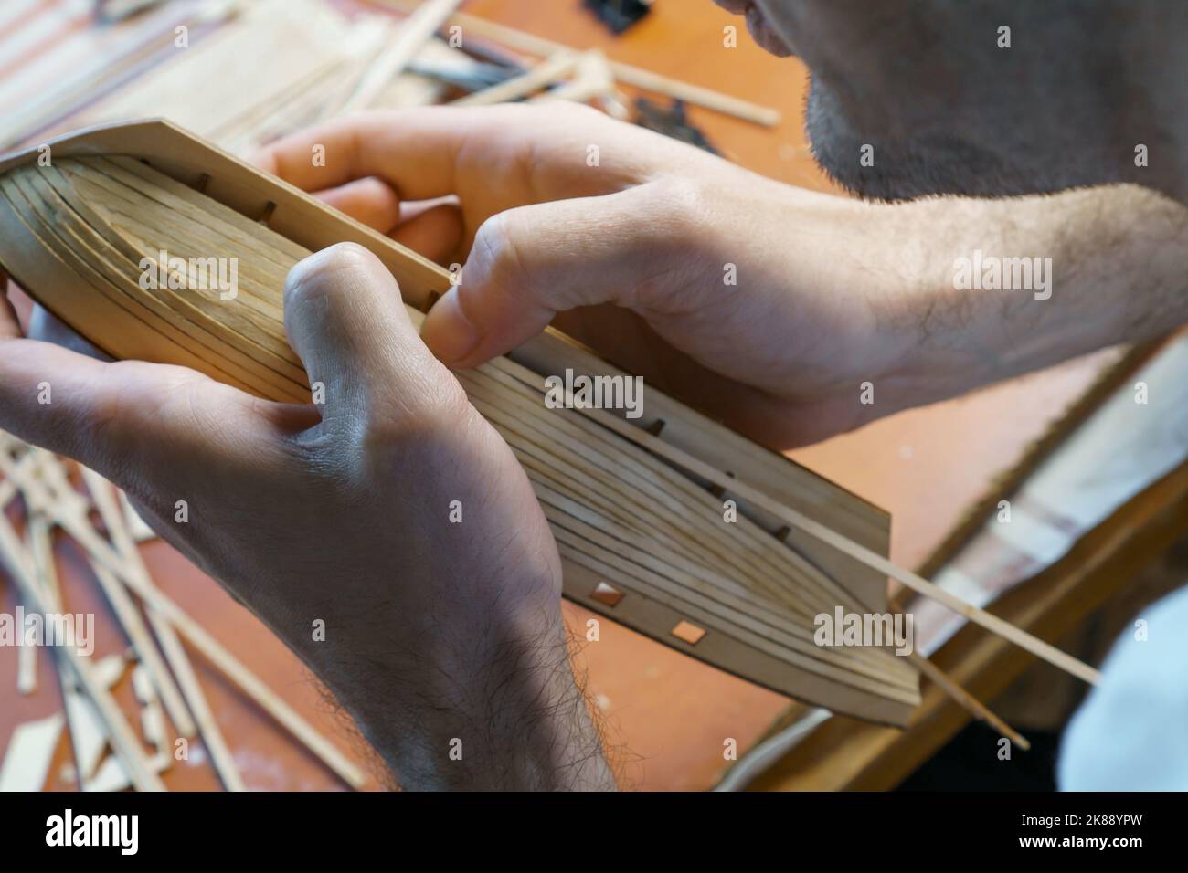 Hands of man gluing plywood details for ship model with glue, holding
