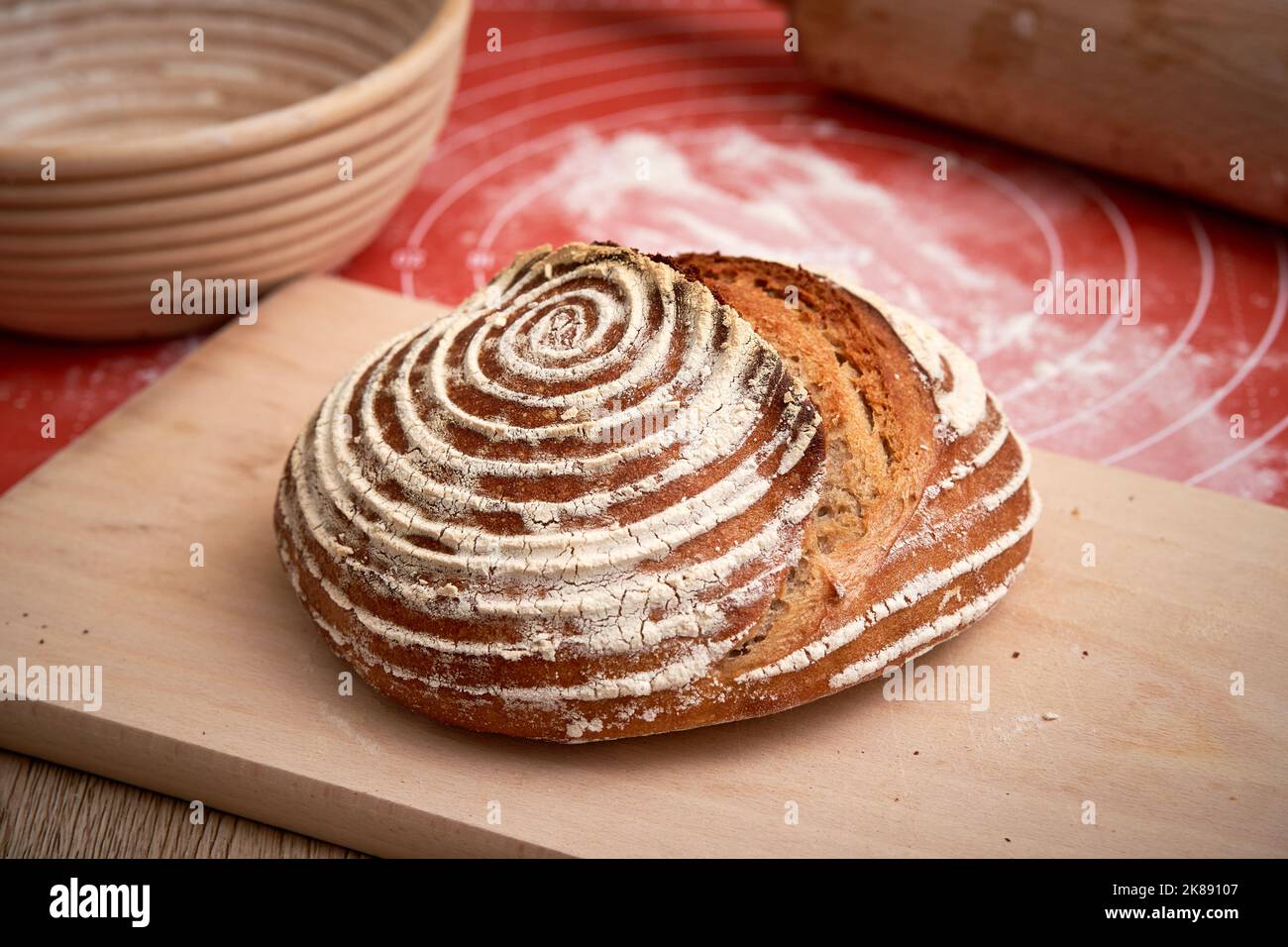 Artisan Sourdough bread baked at home. Beautiful crust of the bread. Cane banneton at the background Stock Photo