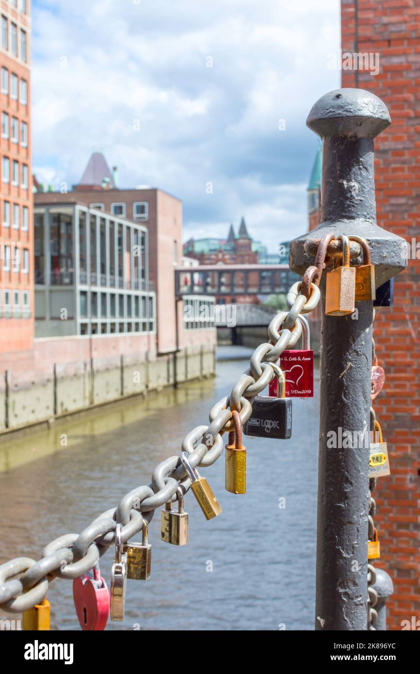 On an old link chain of the Speicherstadt in Hamburg hang many colorful so-called love locks in different shapes. The chain stands out against Stock Photo