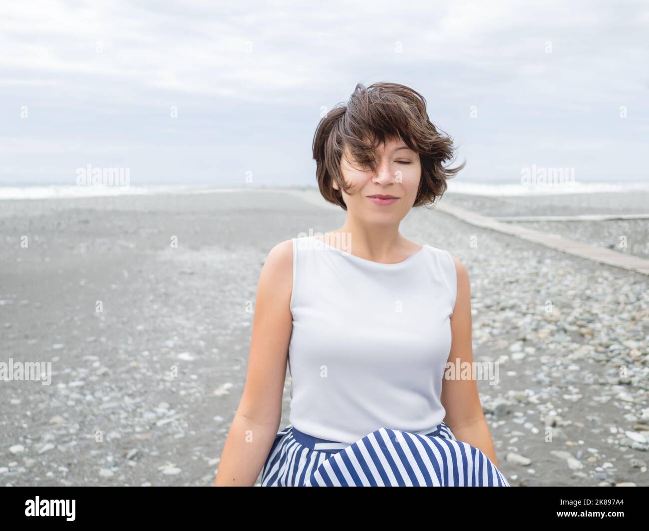 Portrait of smiling woman on seaside. Woman with hair ruffled with the wind. Wanderlust concept. Vacation on sea coast. Stock Photo