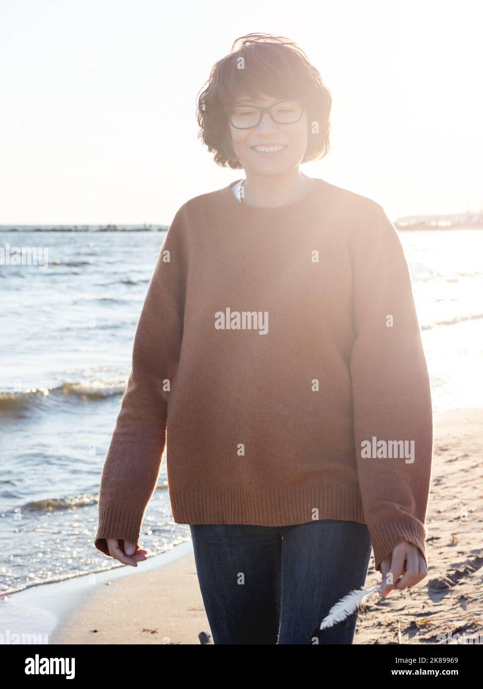 Portrait of smiling woman on seaside. Woman with hair ruffled with the wind. Walking at sunset by the sea. Stock Photo