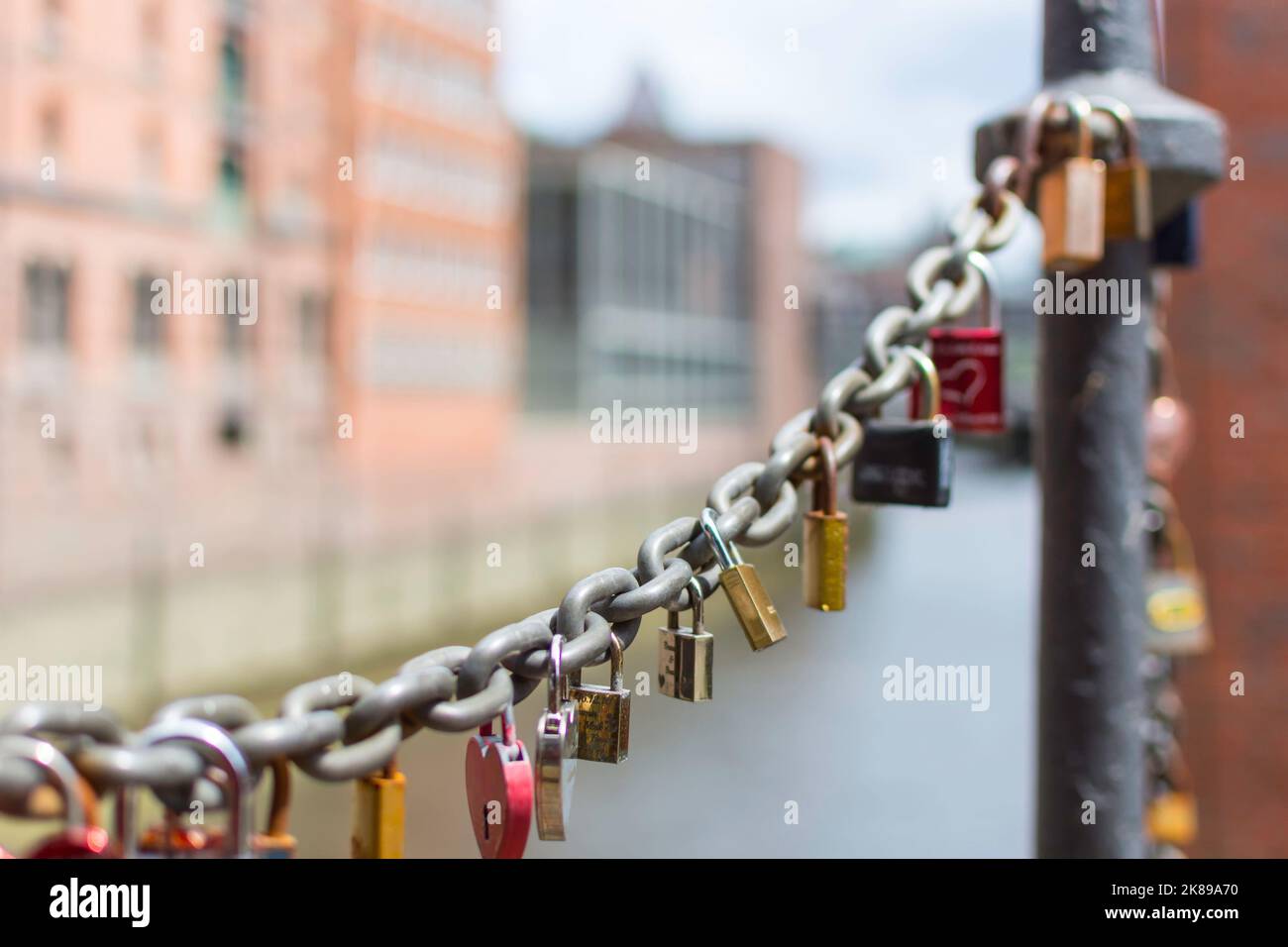 On an old link chain of the Speicherstadt in Hamburg hang many colorful so-called love locks in different shapes. The chain stands out against the Stock Photo